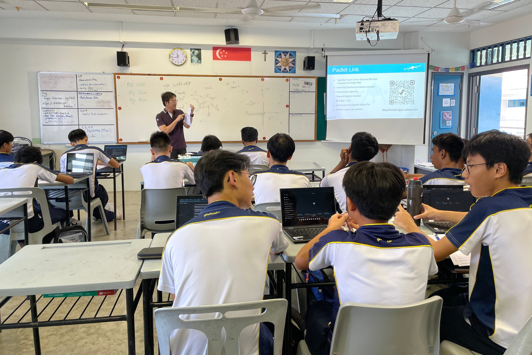 Male teacher stands in front of a whiteboard, addressing to a group of students